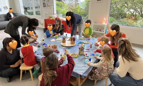 Eltern und Kinder sitzen gemeinsam an einem Tisch beim Basteln und Malen, im Hintergrund eine gemütliche Sofaecke – Event bei Tiny Hands Creations in Zürich