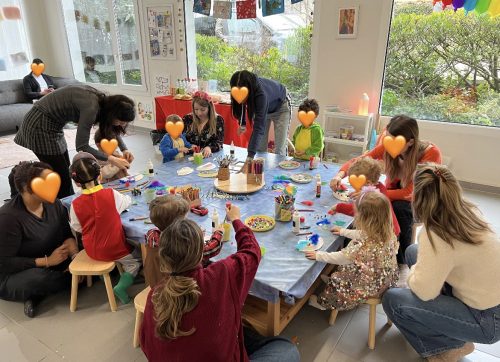 Eltern und Kinder sitzen gemeinsam an einem Tisch beim Basteln und Malen, im Hintergrund eine gemütliche Sofaecke – Event bei Tiny Hands Creations in Zürich