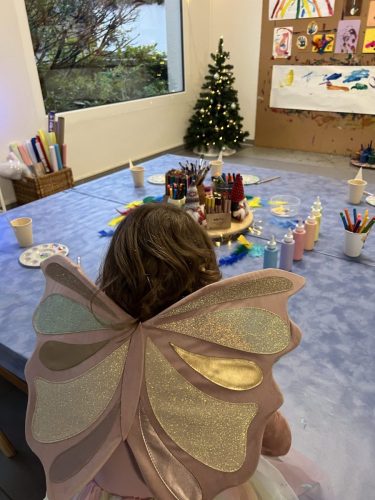 Kind mit Märchenflügeln von hinten, vor dem Basteltisch und der Malwand bei einer Geburtstagsparty im Märchenland-Thema von Tiny Hands Creations