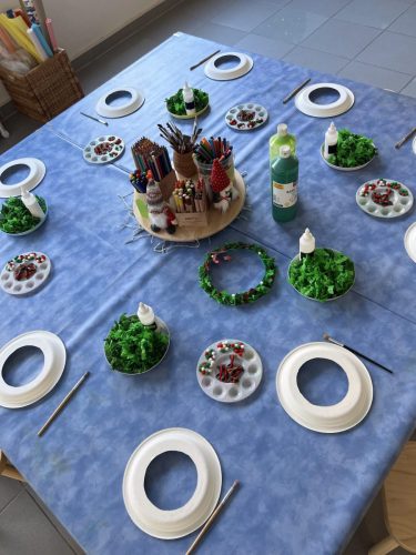 Blick auf den Basteltisch bei einer Dinosaurier-Geburtstagsparty, Kinder gestalten einen Kranz aus Papptellern im Atelier von Tiny Hands Creations