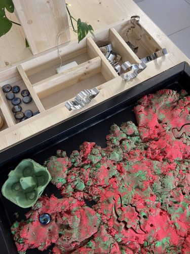 Sensorischer Tisch mit kinetischem Sand, Dinosaurier-Figuren und verschiedenen Formen im Atelier von Tiny Hands Creations