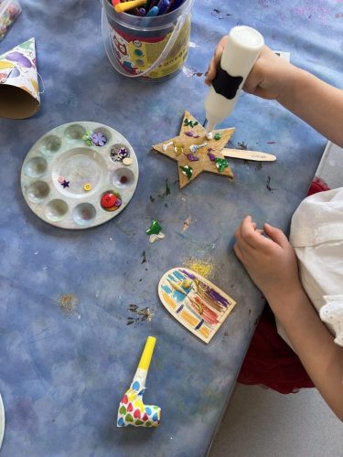 Nahaufnahme vom Basteltisch: Ein Kind verziert einen Zauberstab mit Sternform bei einer Geburtstagsparty im Atelier von Tiny Hands Creations