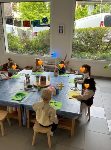Viele Kinder sitzen gemeinsam an einem Tisch und arbeiten an einem Bastelprojekt in der Spielgruppe von Tiny Hands Creations