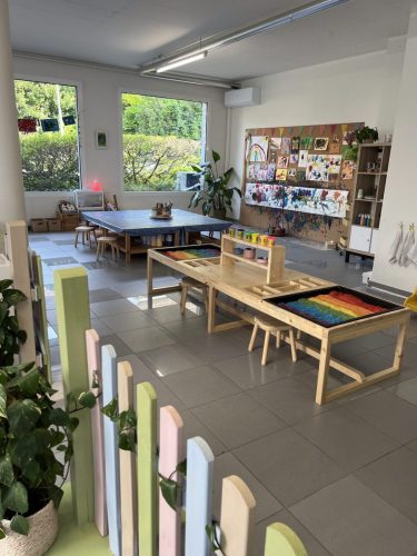 Innenansicht des Ateliers von Tiny Hands Creations mit sensorischem Tisch, Malwand, Basteltisch, Farbzaun, großen Fenstern, Klimaanlage und Pflanzen