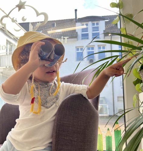 Kind benutzt selbstgebasteltes Fernglas im Eingangsbereich von Tiny Hands Creations und zeigt mit dem Finger auf etwas