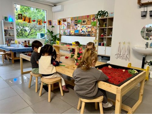 Fünf Kinder experimentieren und spielen am großen sensorischen Tisch in der Spielgruppe in Zürich.