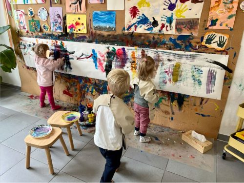 Drei Kinder mit Malschürzen malen an der großen Malwand in der Spielgruppe in Zürich.