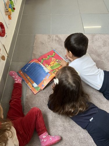 Drei Kinder liegen auf dem Boden in der Bücherecke und schauen sich Bücher in der Spielgruppe in Zürich an.