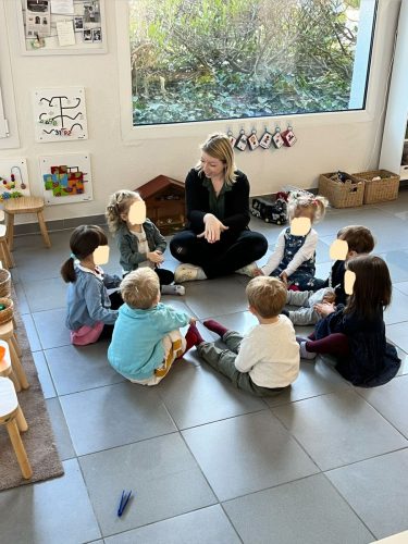 Sieben Kinder sitzen mit der Spielgruppenleiterin auf dem Boden beim Morgenkreis in der Spielgruppe in Zürich.