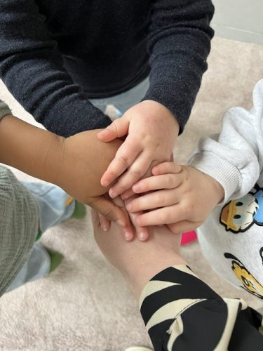 Vier Kinder stapeln ihre Hände in der Mitte des Kreises während einer Gruppenaktivität in der Spielgruppe in Zürich.