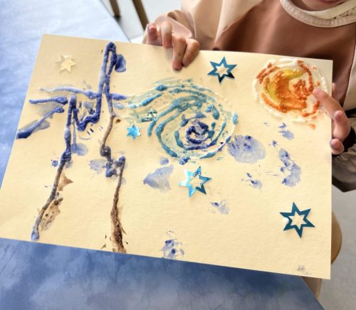 Kind hält stolz ein selbstgestaltetes Kunstprojekt, das ein Van-Gogh-Bild darstellen soll, im Atelier von Tiny Hands Creations